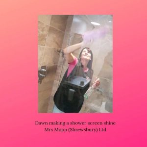 Mrs Mopp Shrewsbury domestic Moppette Dawn cleaning a client's shower screen in a black Mrs Mopp tabard and pink t-shirt, holding a pink microfibre cloth  | Mrs Mopp UK